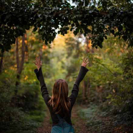 woman wearing black sweater and denim overalls standing under leaves